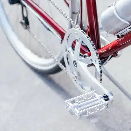 Nahaufnahme einer silbernen Kurbelgarnitur, eines silbernen Pedals und einer silbernen Fahrradkette an einem roten Fahrradrahmen.