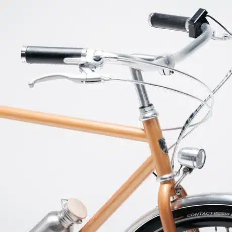 Nahaufnahme des Lenkers mit Bremshebeln, Griffen und einem Teil des Rahmens eines bronzefarbenen E-Bikes.