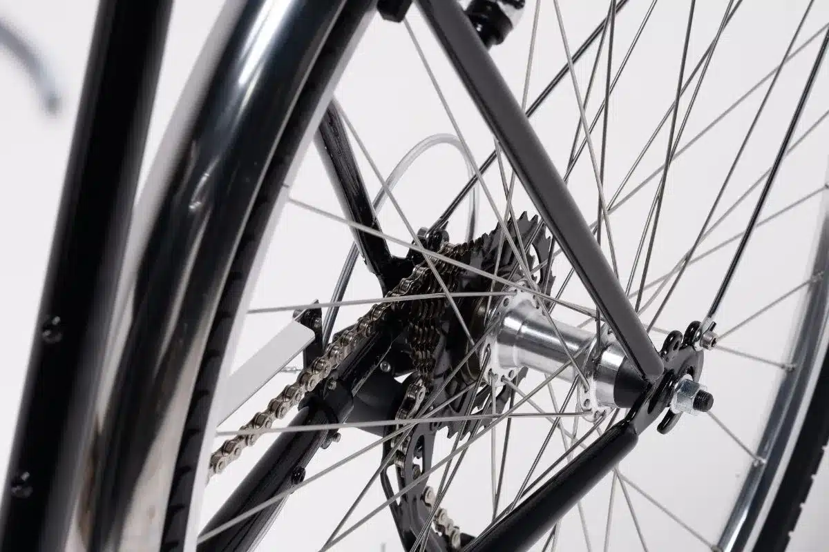 Nahaufnahme des Hinterrads eines schwarzen Fahrrads mit sichtbarer 7-Gang-Shimano-Schaltung, silberner Nabe und vielen Speichen.