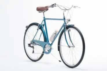 Blaues Capri Vienna Electric E-Bike mit braunem Ledersattel und silberner Wasserflasche, ausgestellt vor weißem Hintergrund.
