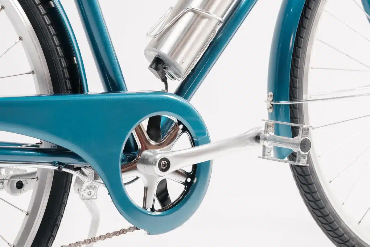 Detailaufnahme eines türkisfarbenen Capri Vienna Electric E-Bikes mit Fokus auf den Antriebsstrang, inklusive Kurbel, Kettenblatt und Kette.