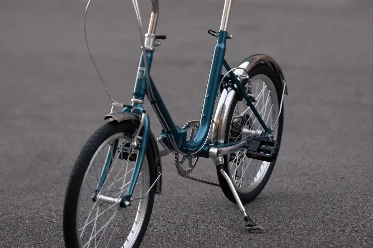 Detailaufnahme eines Capri Vita Falt-E-Bikes in Petrol, Vorderansicht von der Seite mit Fokus auf das Rad, den Rahmen und den Ständer.