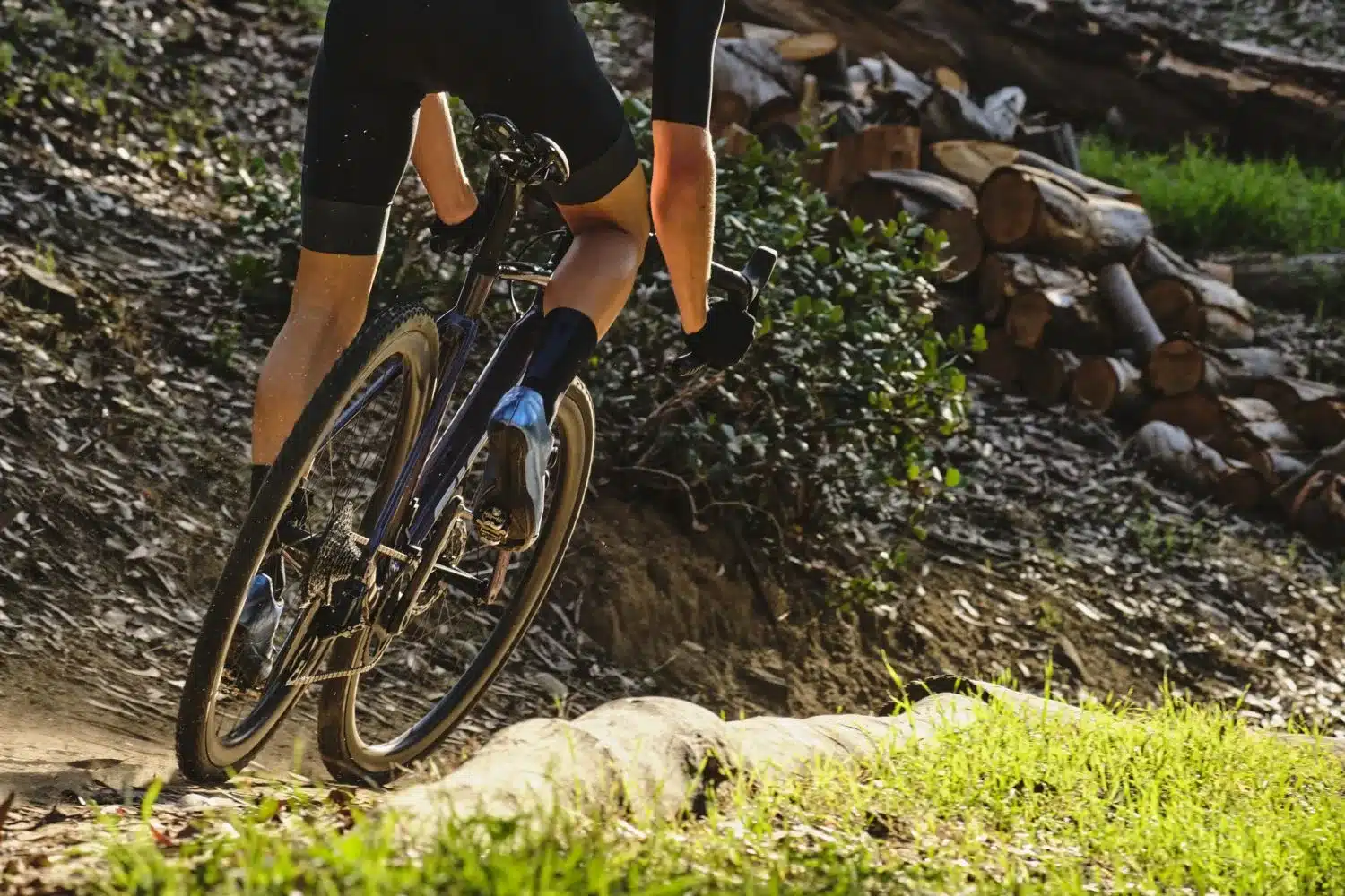 Fahrer in Schwarz auf einem Rennrad auf einem Waldweg, das Bild zeigt die Hinterräder und den Unterkörper.