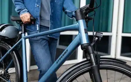 Person im Jeans-Outfit steht neben einem blauen Stevens Aviolo 8.1 HT Tourenrad, Fokus auf den Rahmen mit dem Markennamen Stevens und die Vorderradgabel.