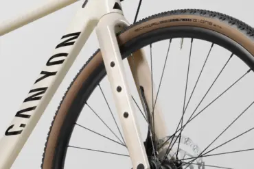 Nahaufnahme des Vorderteils eines cremefarbenen Canyon Fahrrads, das den Rahmen, die Gabel und das Vorderrad mit braunen Reifen zeigt.