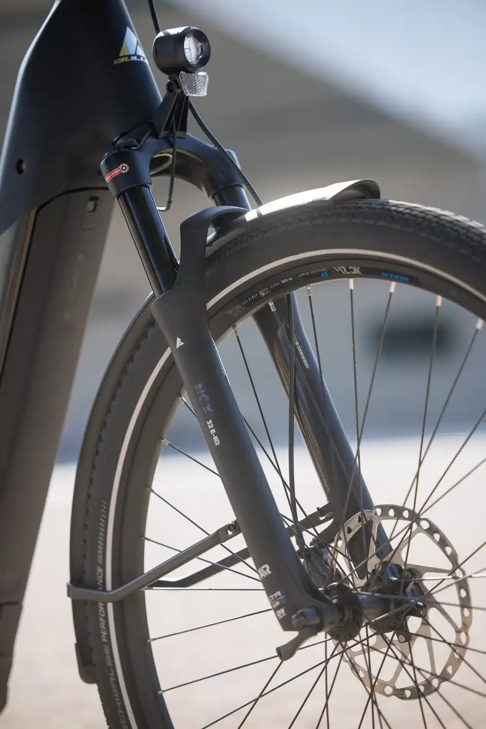 Nahaufnahme der Vorderradgabel eines schwarzen Bulls Cross Lite EVO Carbon E-Bikes mit Federung, Scheibenbremse, Reifen mit Schwalbe Bereifung und integriertem Scheinwerfer.