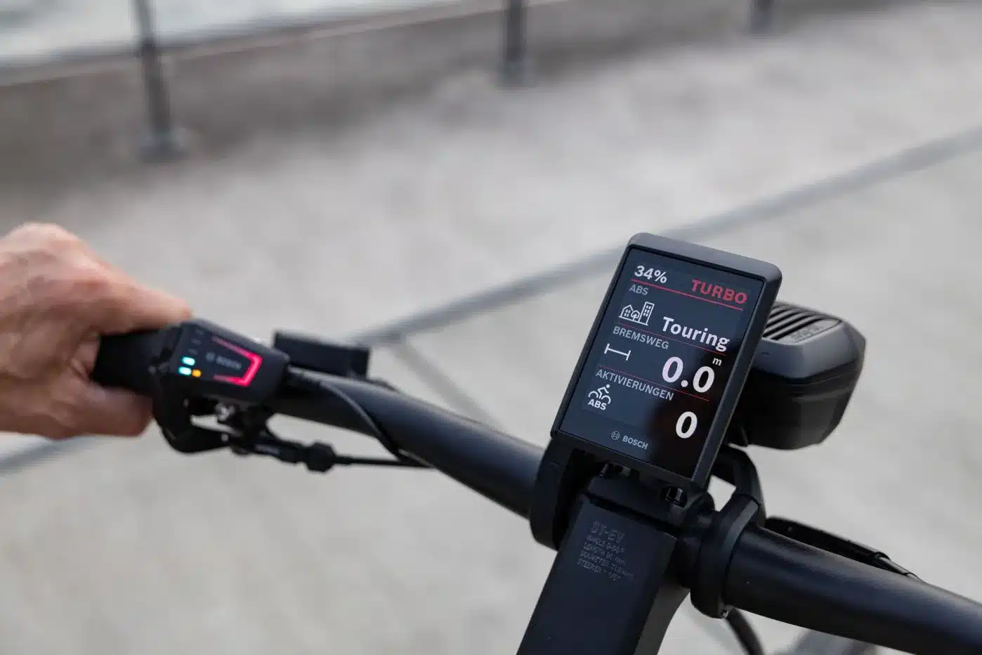 Nahaufnahme des Displays und der Bedieneinheit eines E-Bikes, das den Fahrmodus 'Turbo' und 'Touring' sowie den Akkustand anzeigt.