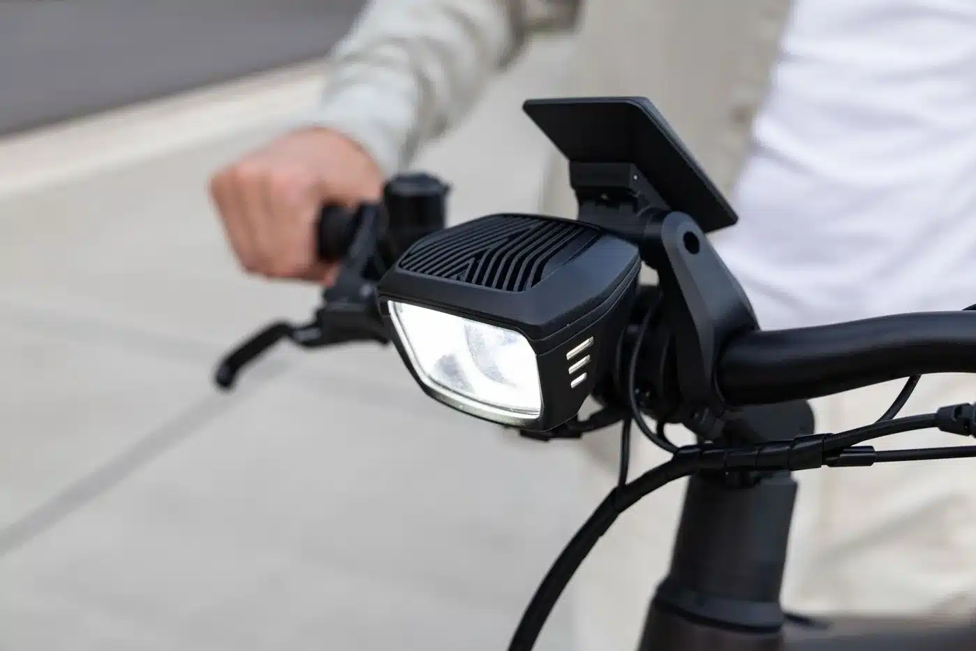 Nahaufnahme eines Fahrradlenkers mit einem modernen, hell leuchtenden Scheinwerfer und dem Griff, den eine Hand hält.