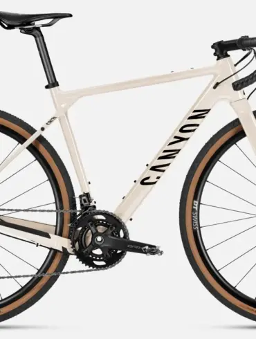 Canyon Grizl AL 7 Gravel-Bike in heller Sandfarbe mit schwarzen Akzenten, ausgestattet mit DT Swiss Laufrädern und Schwalbe G-One Reifen.