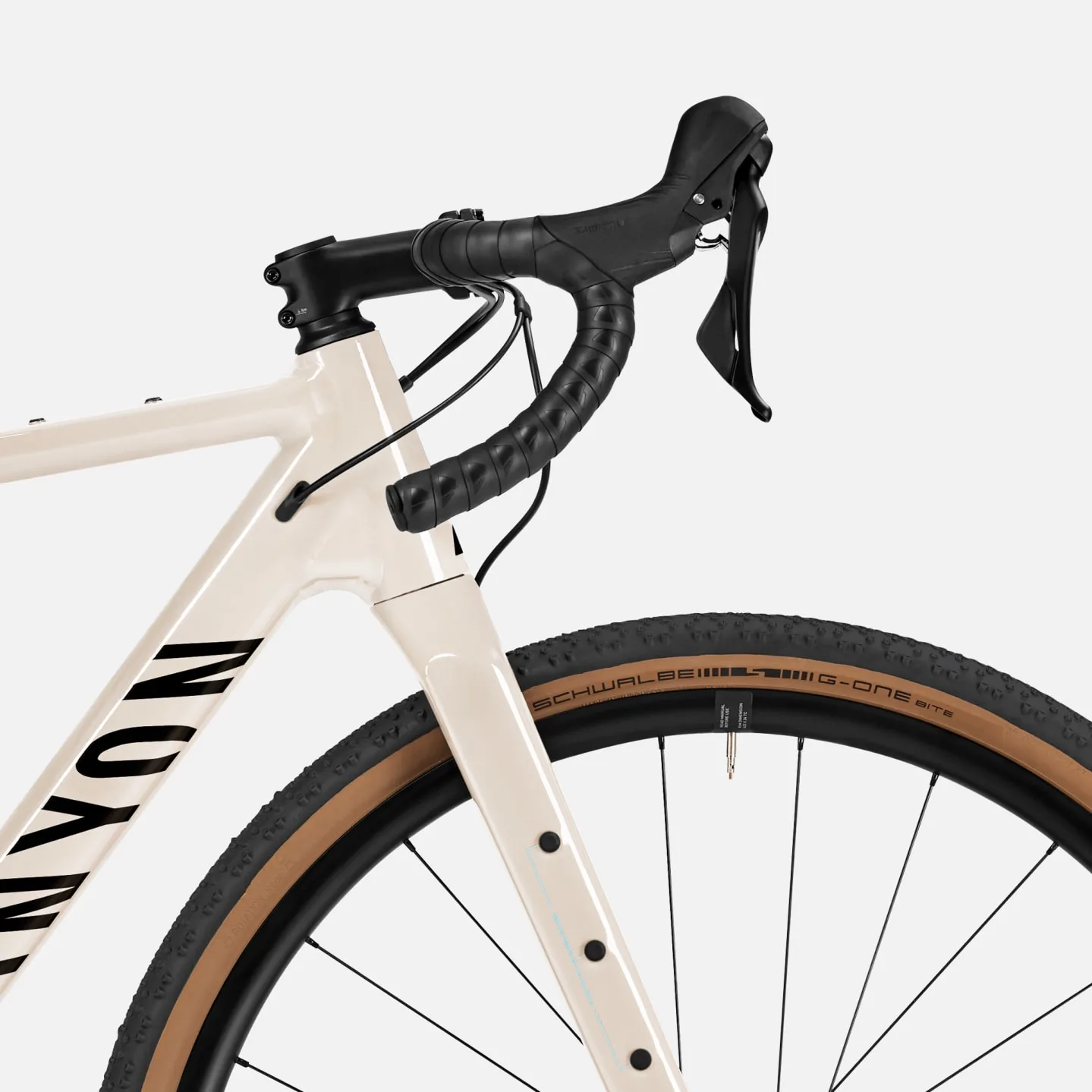 Detailaufnahme eines cremefarbenen Canyon Grizl AL 7 Gravel-Bikes, das den vorderen Teil des Rahmens, den schwarzen Lenker mit Schaltgriffen und ein Teil des Rades mit einem Schwalbe G-One Bite Reifen zeigt.