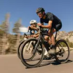 Zwei Radfahrer in sportlicher Haltung auf E-Gravelbikes im Freien mit felsigen Bergen und Bäumen im Hintergrund