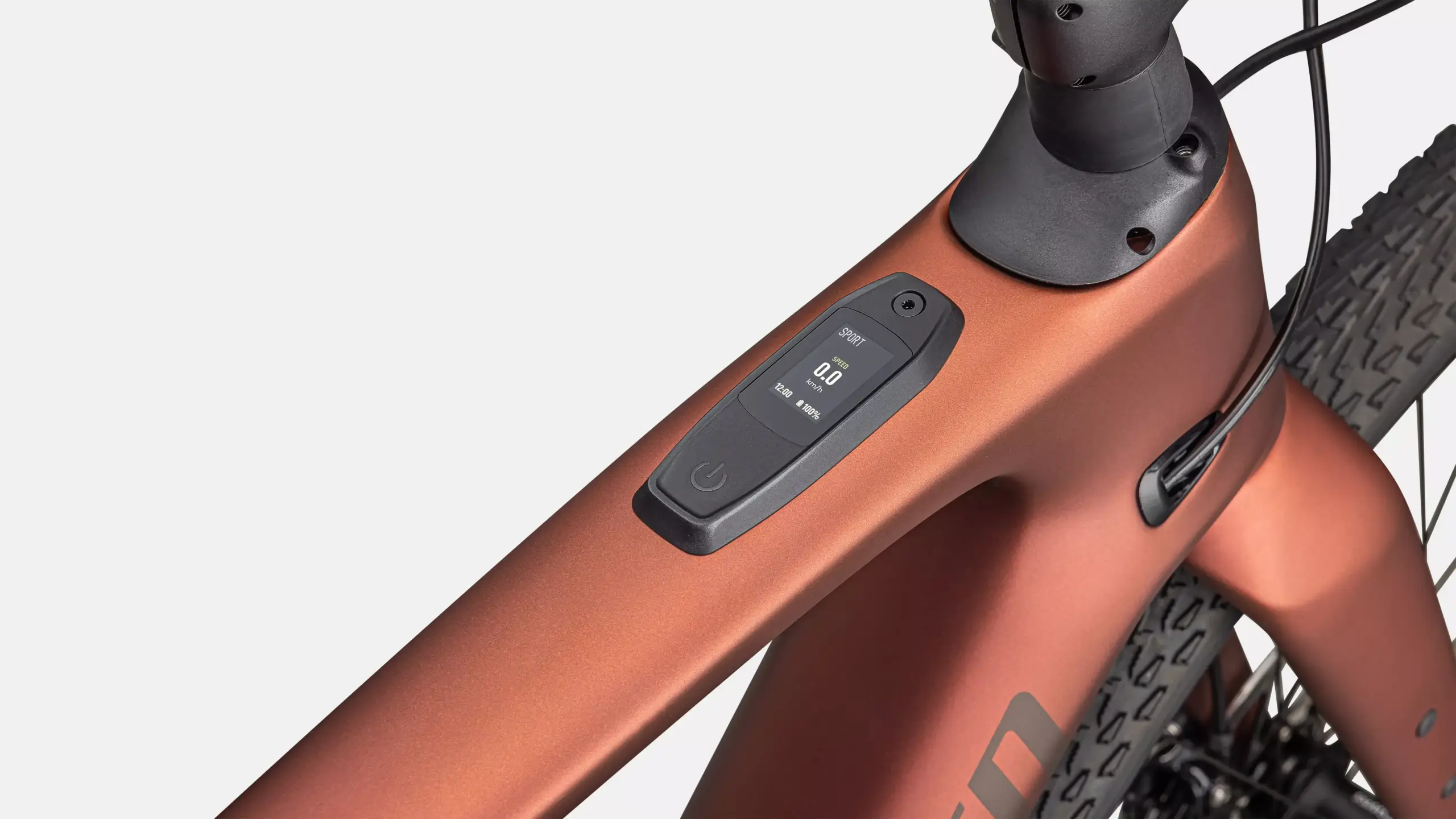 Detailaufnahme des Displays mit Geschwindigkeit (0.0 km/h), Uhrzeit (12:00) und Akkuladestand (100%) auf dem kupferfarbenen Rahmen eines Specialized Turbo Creo 2 Expert E-Gravelbikes.