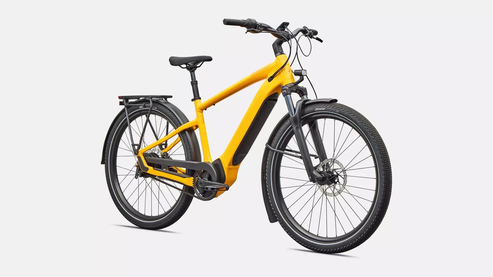 Frontale Ansicht eines gelben Specialized Turbo Vado 4.0 IGH E-Bikes mit schwarzem Gepäckträger, Federgabel und Schutzblechen, stehend vor weißem Hintergrund.