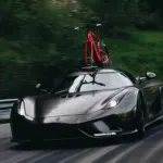 Schwarzer Sportwagen mit rotem Rennrad auf dem Dach auf einer asphaltierten Straße.