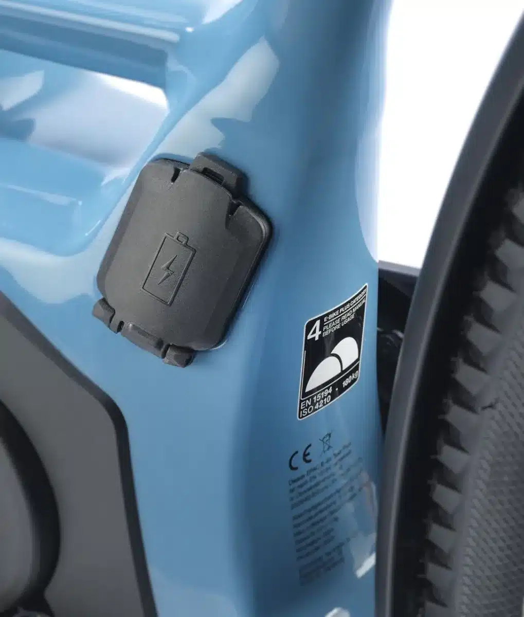 Nahaufnahme des blauen Rahmens eines STEVENS E-8X Tour Plus Forma E-Bikes, mit Fokus auf den Ladeanschluss und einem Hinweisschild zur maximalen Belastung.
