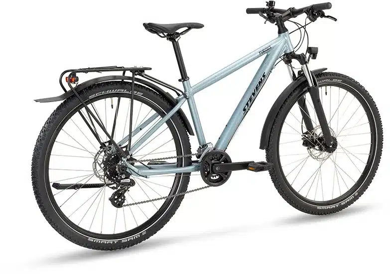 Seitenansicht eines hellblauen Stevens Furious Tour 27.5 Fahrrads mit Gepäckträger, Schutzblechen und Federgabel.