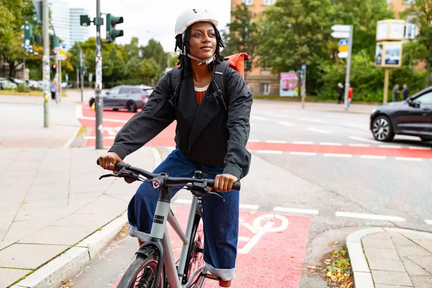 Frau mit Helm und Rucksack fährt ein Stevens Kalea 7.1 LT Fahrrad auf einer Straße mit Fahrradspur.