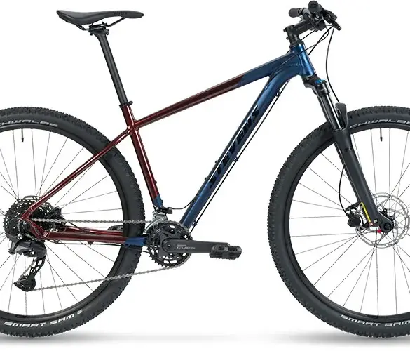 Seitenansicht eines Stevens Taniwha Mountainbikes mit blau-rotem Rahmen, 29-Zoll-Rädern und Federgabel.