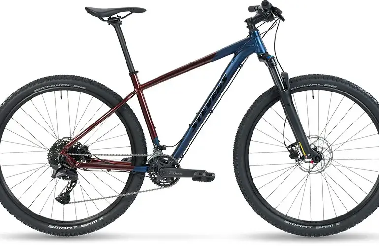 Seitenansicht eines Stevens Taniwha Mountainbikes mit blau-rotem Rahmen, 29-Zoll-Rädern und Federgabel.