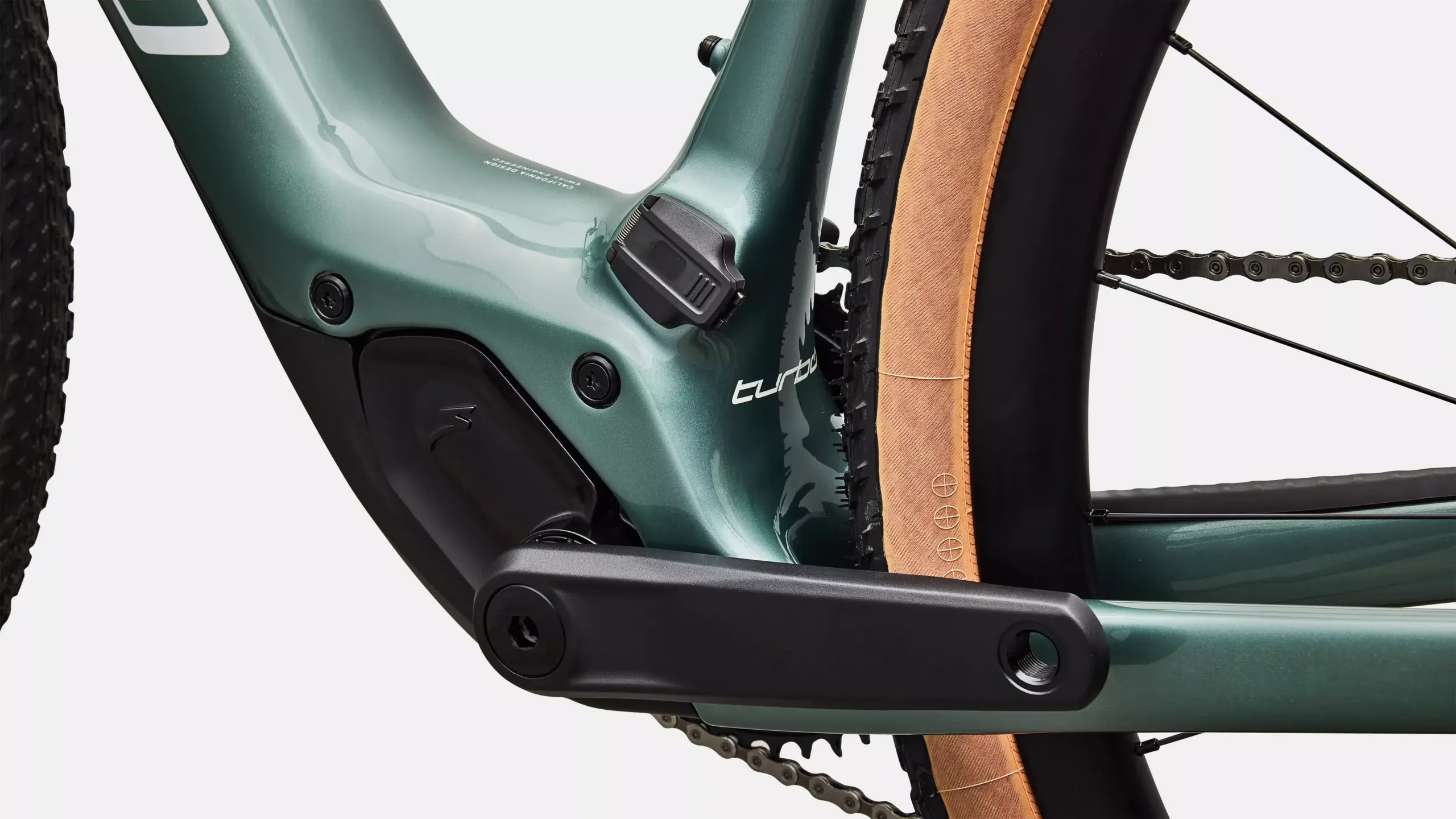 Nahaufnahme des grünen Carbonrahmens eines Specialized Turbo Creo 2 Expert E-Gravelbikes, mit Fokus auf das Tretlagerbereich, die Kurbelgarnitur und den breiten Gravel-Reifen mit brauner Seitenwand.