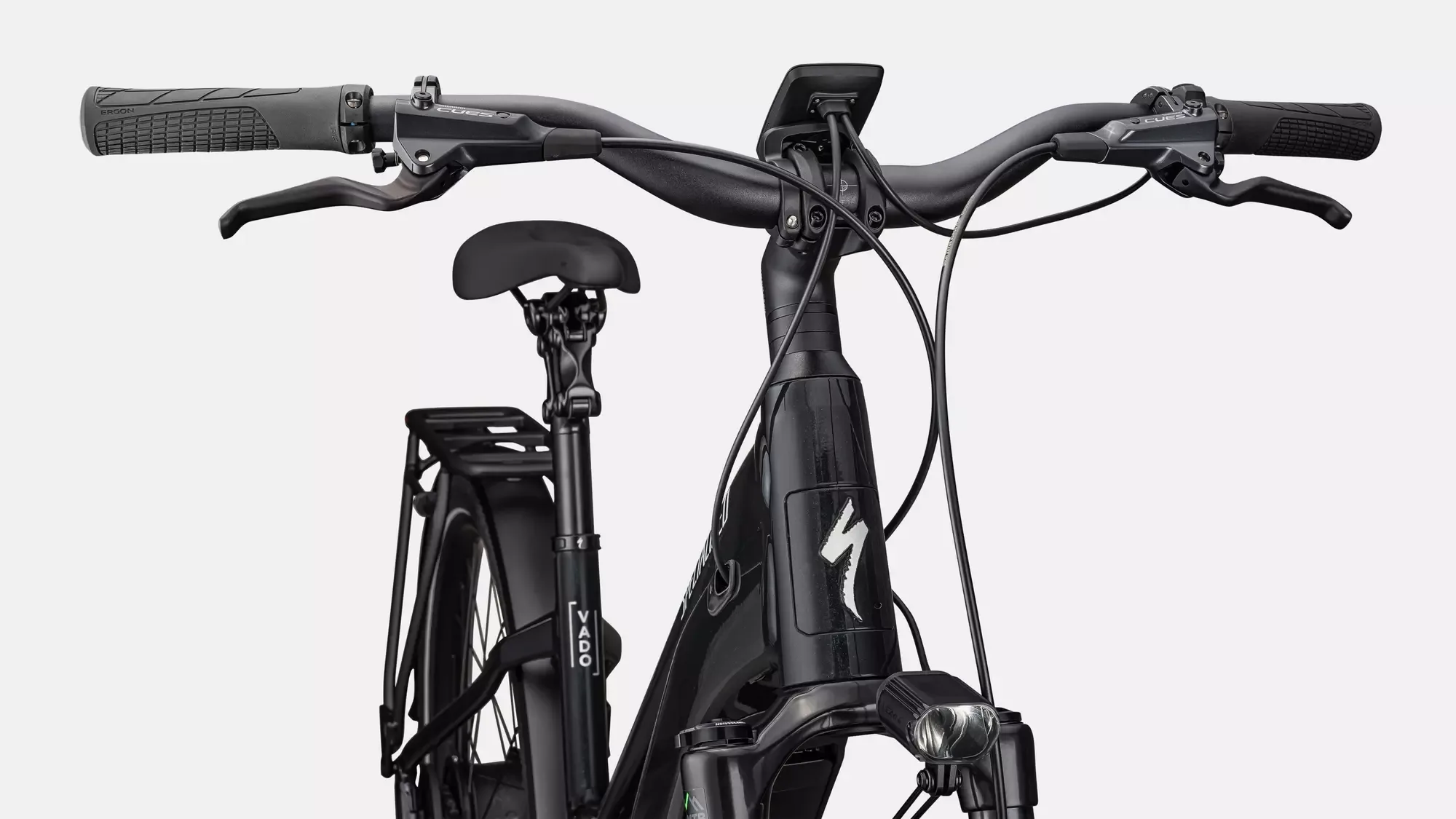 Nahaufnahme des schwarzen Specialized Turbo Vado 5.0 IGH Step-Through E-Bikes, das die Details des Lenkers, des Displays, der Vorderseite des Rahmens mit dem markanten Specialized-Logo und der integrierten Beleuchtung zeigt.