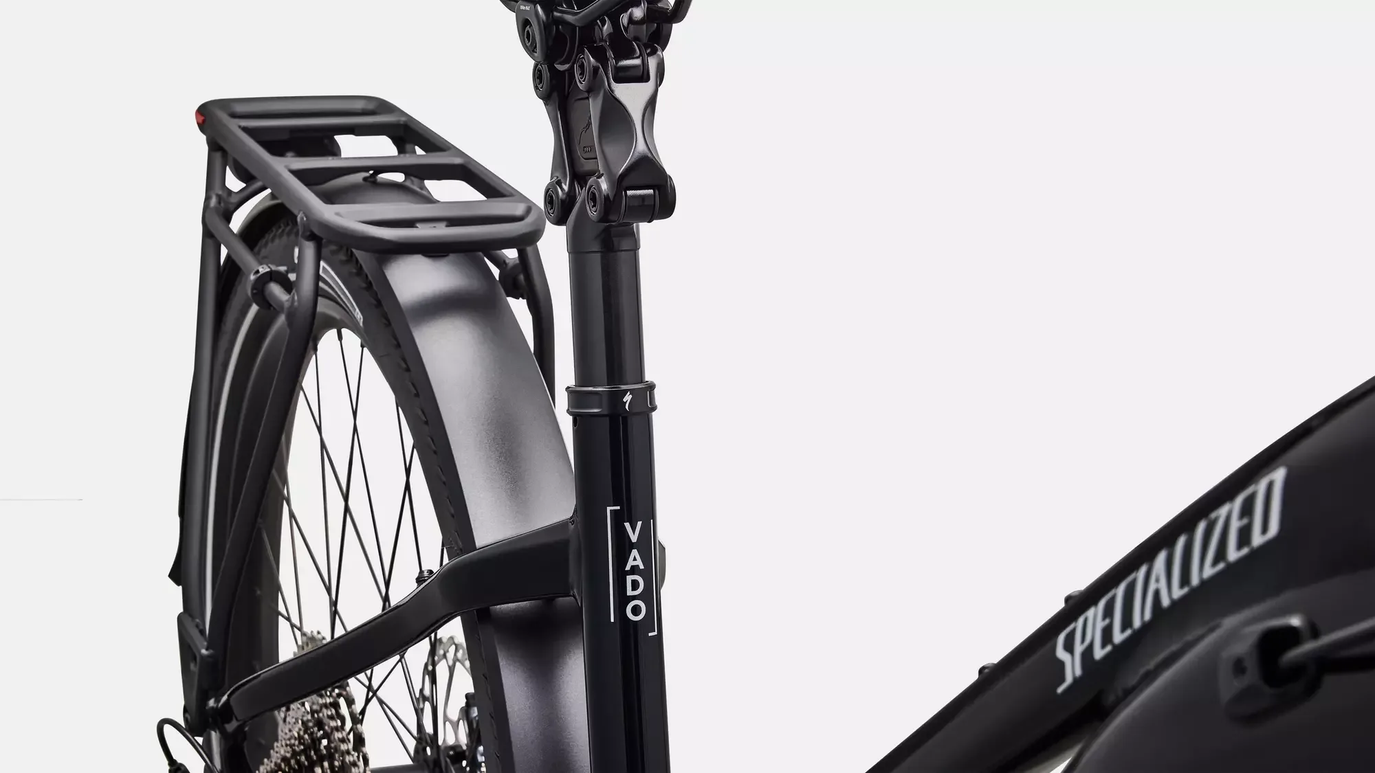 Detailansicht eines schwarzen Specialized Turbo Vado 5.0 Step-Through E-Bikes mit Fokus auf die Sattelstütze, den Gepäckträger und das Hinterrad.