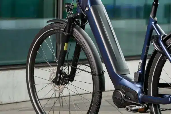 Nahaufnahme des Vorderrads, der Federgabel und des Unterrohrs mit integriertem Akku eines blauen Giant DailyTour E+ 2 GTS E-Bikes. Deutlich erkennbar sind Schutzblech, Bremsscheibe und Motor. Das Rad ist für den täglichen Einsatz konzipiert.