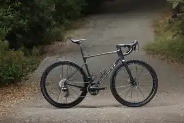 Giant Defy Advanced SL 0 Endurance-Rennrad in dunklem Grau, das seitlich auf einer Straße steht, umgeben von Bäumen und Laub.