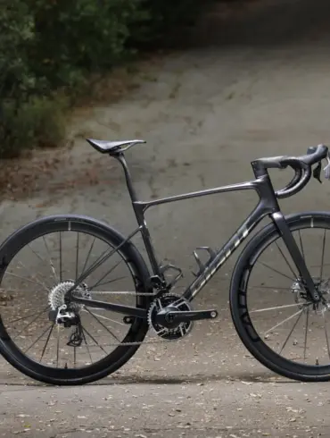 Giant Defy Advanced SL 0 Endurance-Rennrad in dunklem Grau, das seitlich auf einer Straße steht, umgeben von Bäumen und Laub.