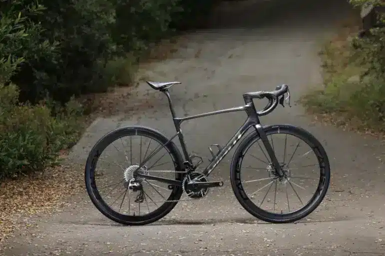 Giant Defy Advanced SL 0 Endurance-Rennrad in dunklem Grau, das seitlich auf einer Straße steht, umgeben von Bäumen und Laub.