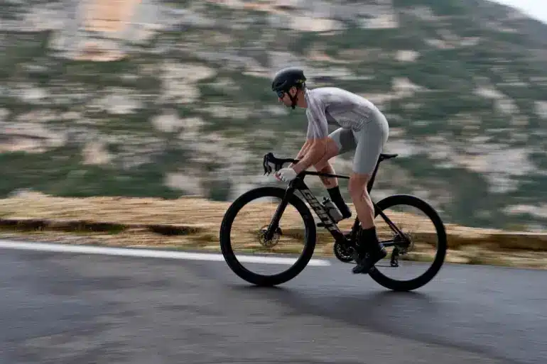 Radfahrer fährt schnelles Aero-Rennrad Giant Propel Advanced Pro auf kurviger Straße mit Bergkulisse.