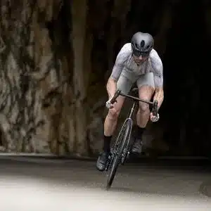 Radfahrer mit Helm und Rennradbekleidung fährt auf einem schnellen Rennrad durch einen felsigen Tunnel, die Front des Fahrrads ist nach vorne geneigt.