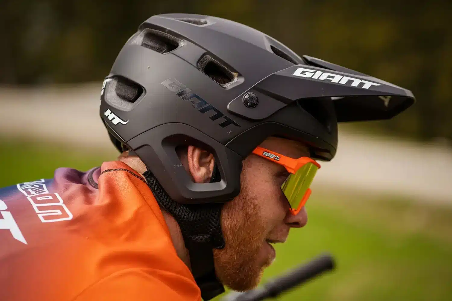 Schwarz matter Giant Realm MIPS Fahrradhelm mit orangenem Visier und Brille auf dem Kopf eines Mannes.