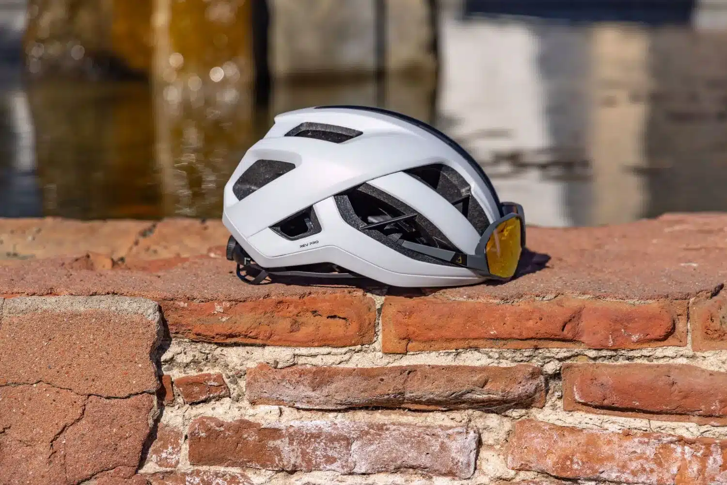 Weißer Giant Rev Pro Rennradhelm mit integrierter Sonnenbrille, liegend auf einer Ziegelmauer.