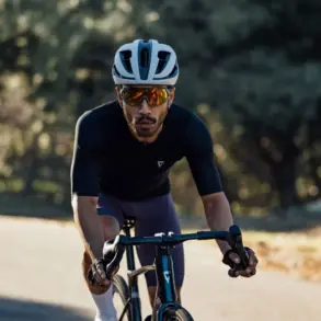 Radsportler mit weißem Giant Rev Pro Helm und Sonnenbrille fährt auf einem Rennrad auf einer Straße.