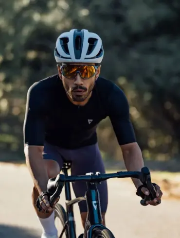 Radsportler mit weißem Giant Rev Pro Helm und Sonnenbrille fährt auf einem Rennrad auf einer Straße.
