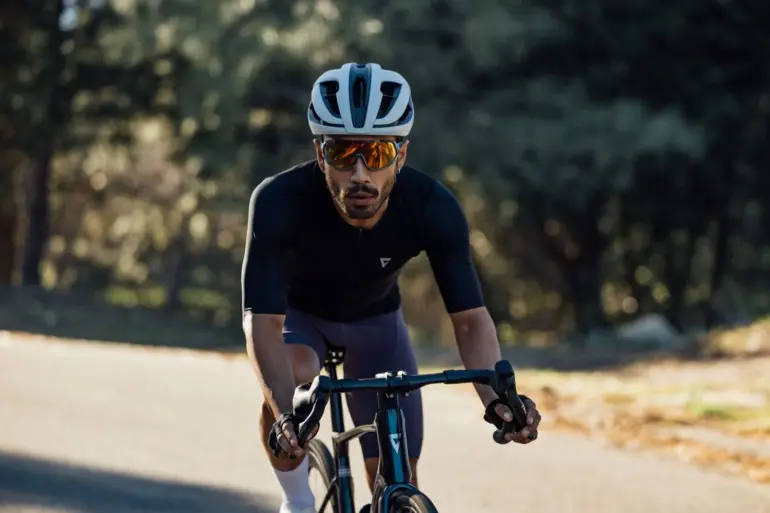 Radsportler mit weißem Giant Rev Pro Helm und Sonnenbrille fährt auf einem Rennrad auf einer Straße.