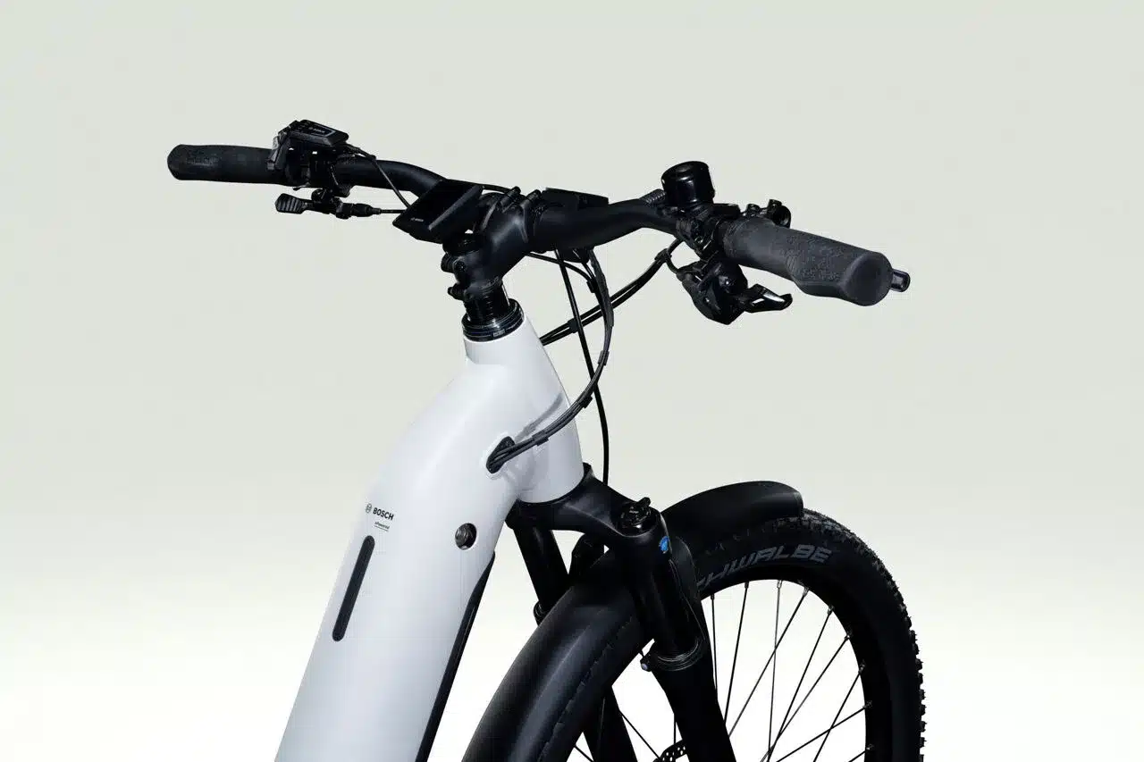 Nahaufnahme des weißen Rahmens, des schwarzen Lenkers mit Bedienelementen und des Vorderbaus mit Federgabel und Rad eines Lapierre E-Explorer 8.8 Low E-Trekkingbikes.