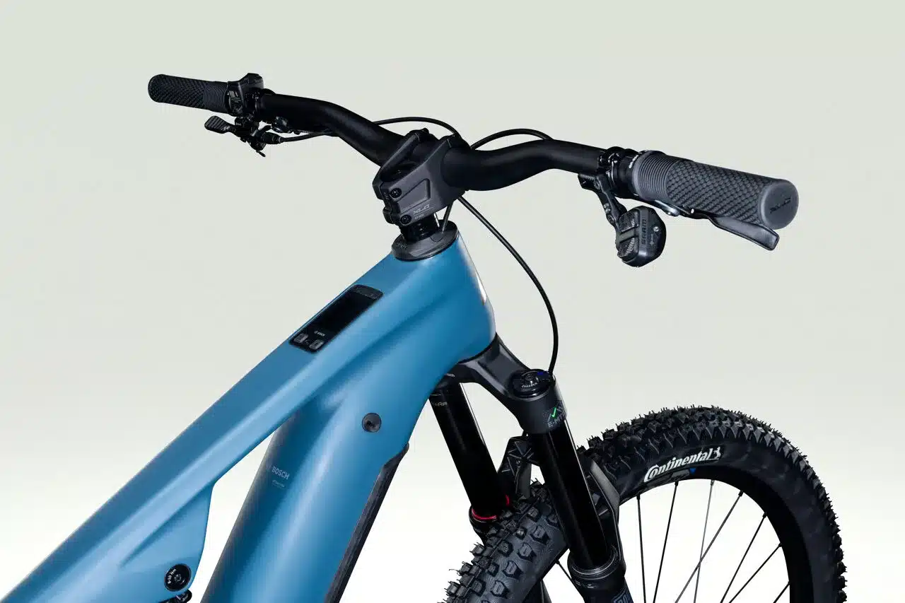 Detailansicht des blauen Overvolt AM CF 7.8 E-MTBs mit Fokus auf Lenker, Gabel und den oberen Teil des Rahmens.