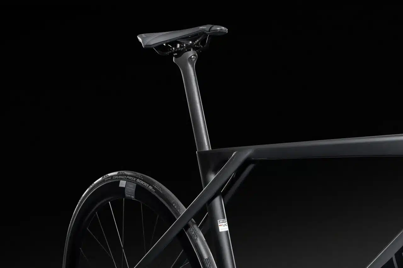 Eine Nahaufnahme zeigt das schwarze Carbon-Sitzrohr und den Sattel eines Lapierre Xelius DRS 9.0 Rennrads. Ein Teil des Hinterrads mit einem Continental Grand Prix 5000 S TR Reifen ist ebenfalls sichtbar.
