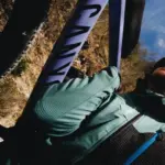 Nahaufnahme einer Frau mit Helm, die auf einem Fahrrad sitzt und ein grün-blaues Longsleeve von Millet trägt, im Hintergrund ein Fahrradrahmen mit der Aufschrift "CANYON".