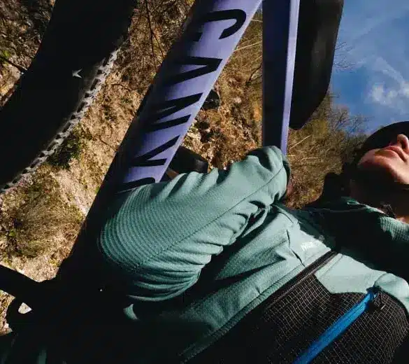 Nahaufnahme einer Frau mit Helm, die auf einem Fahrrad sitzt und ein grün-blaues Longsleeve von Millet trägt, im Hintergrund ein Fahrradrahmen mit der Aufschrift "CANYON".