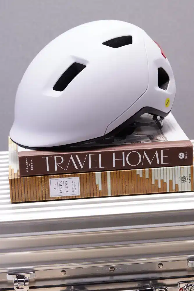 Weißer Novo Mips Fahrradhelm liegt auf Büchern, ein integriertes rotes Rücklicht ist erkennbar.