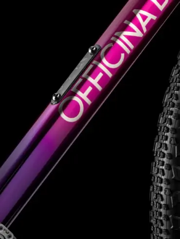 Detailaufnahme eines Fahrradrahmens mit dem Schriftzug OFFICINA in weiß und einem Farbverlauf von Lila zu Pink.