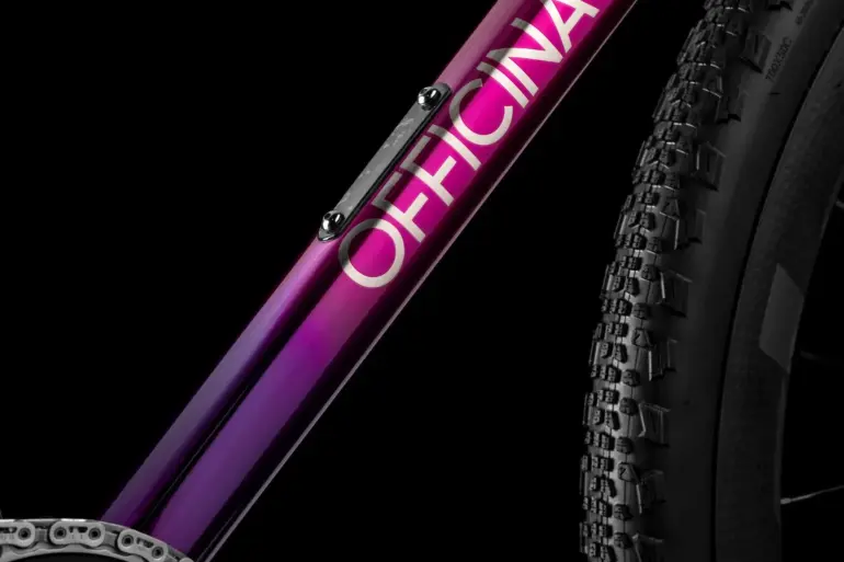 Detailaufnahme eines Fahrradrahmens mit dem Schriftzug OFFICINA in weiß und einem Farbverlauf von Lila zu Pink.
