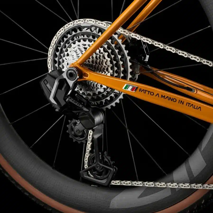 Detailaufnahme des Hinterrads eines Officina Battaglin Matera Gravelbikes mit Fokus auf das Schaltwerk und die Kassette. Der orangefarbene Stahlrahmen trägt die Aufschrift