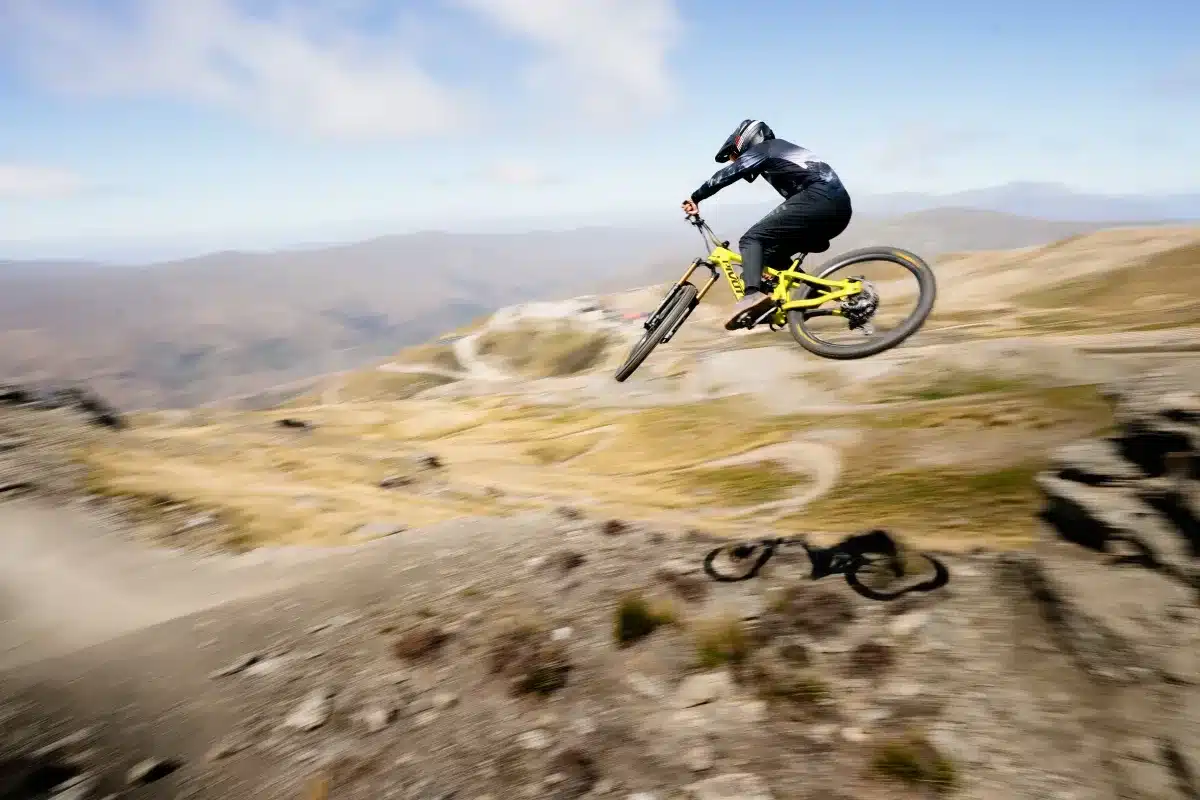 Ein Mountainbiker springt in der Luft mit einem gelben Pivot Firebird Fahrrad über eine hügelige Landschaft.