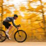 Ein Mann in voller Fahrt auf einem weißen Mountainbike mit Rennlenker, umgeben von verschwommenen gelben Herbstblättern.