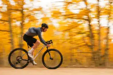 Ein Mann in voller Fahrt auf einem weißen Mountainbike mit Rennlenker, umgeben von verschwommenen gelben Herbstblättern.