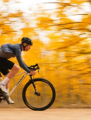 Ein Mann in voller Fahrt auf einem weißen Mountainbike mit Rennlenker, umgeben von verschwommenen gelben Herbstblättern.